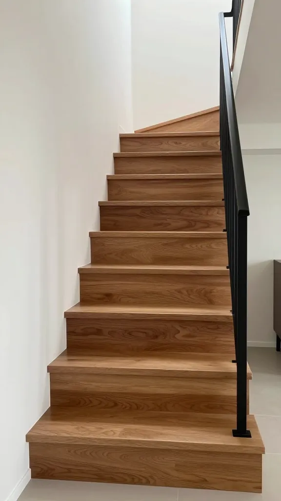 A high-quality, realistic photograph of a stylish small space staircase designed in a Mid-Century Modern aesthetic. The staircase features open risers with warm, medium-toned walnut wood treads, each extending slightly past the base. A sleek, minimalist black metal railing provides a clean, uncluttered look, complementing the staircase's elegant simplicity and clean lines within a bright, contemporary home interior.